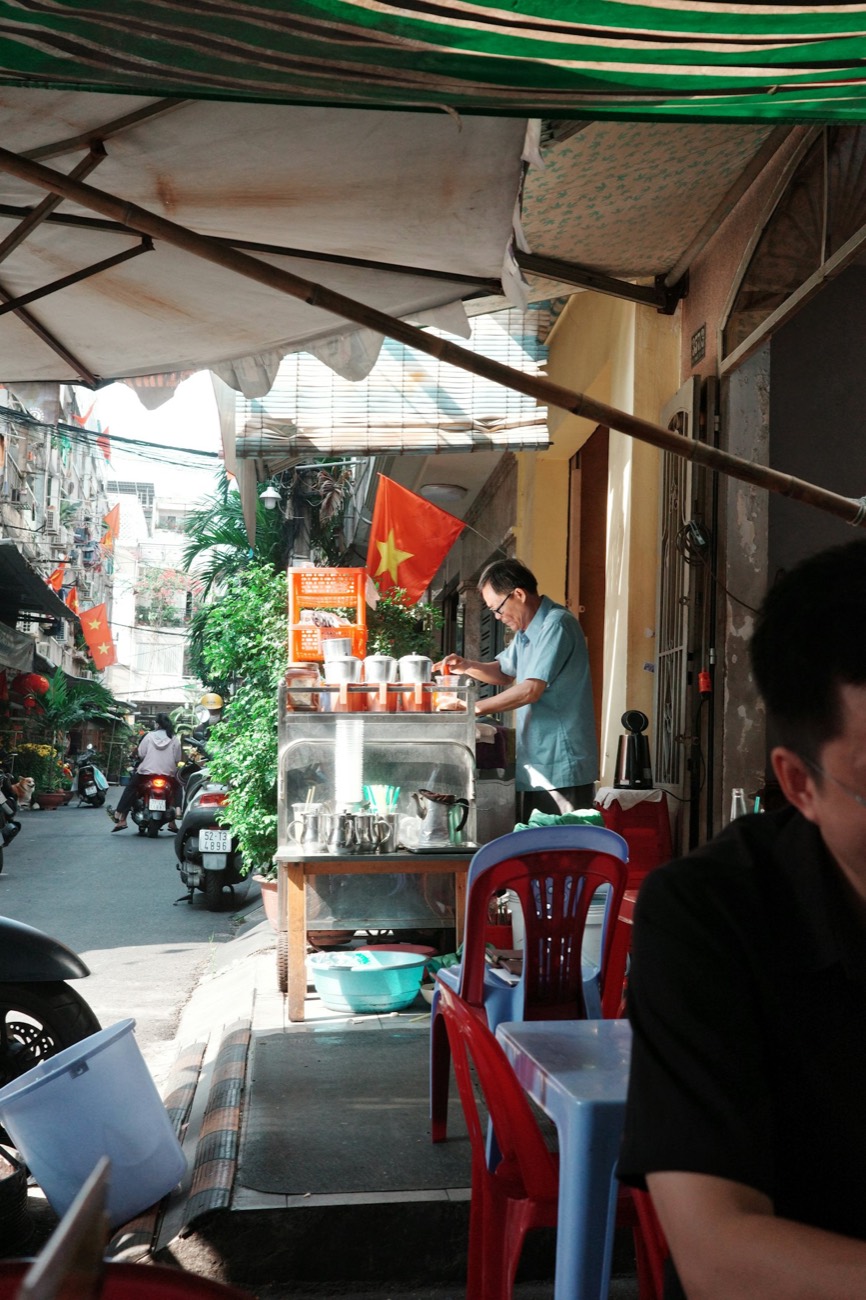 A sidewalk coffee cart with red plastic stools in a Saigon alley