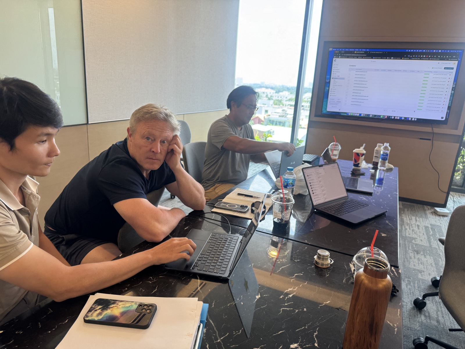A working session at a riverside table, the Saigon skyline through the window